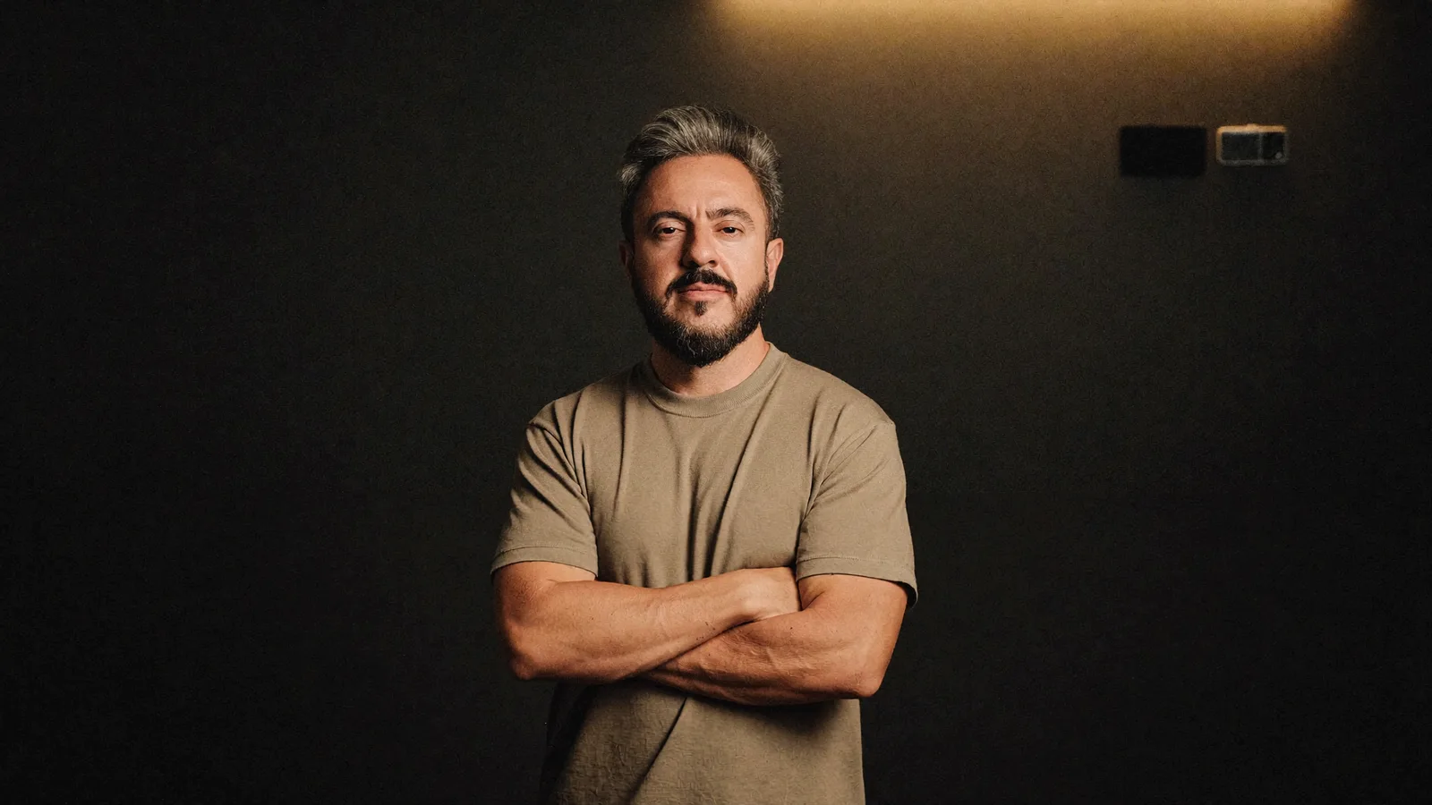 William Motta em pé, braços cruzados, iluminação dourada, ilustrando a preparação da loja para ser a resposta de compra escolhida por um agente de IA